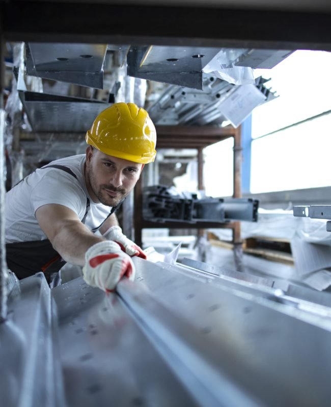 Factory worker working in warehouse handling metal material for production.